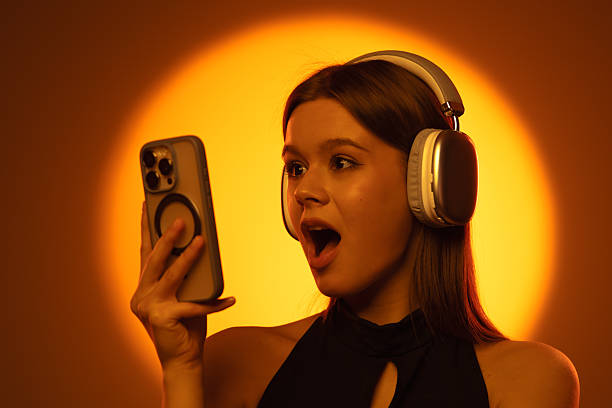 istock Surprised Woman Using Smartphone and Headphones with Bright Background 2225181127