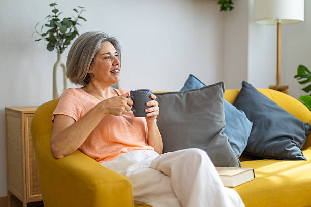 istock Smiling mature woman relaxing on sofa with hot drink 2225182096
