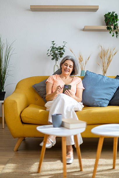 istock Smiling senior woman using smartphone on sofa at home 2225182108