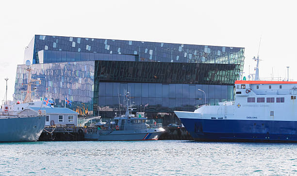 Reykjavik, Iceland - April 4, 2017: Striking waterfront view featuring contemporary building architecture with glass facade, docked ships, and a serene harbor. Harpa Concert Hall is on the background