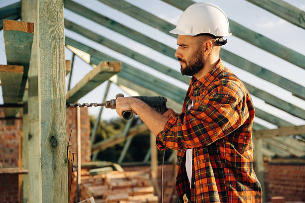 Modern electrical drill. Construction worker is on the roof of a house.