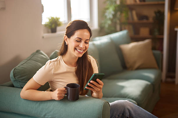 istock Young woman relaxing on sofa, enjoying coffee and browsing smartphone at home 2225197834