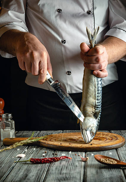 istock A chef holds a freshly caught fish with one hand while expertly filleting it with a knife in a cozy kitchen. Various spices and herbs surround the wooden cutting board, creating a vibrant atmosphere 2225201784