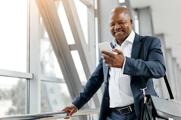 istock Smiling black businessman checking smartphone while leaning against airport railing 2225204508