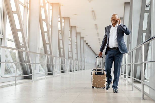 istock Black businessman walking through airport while talking on the phone, pulling suitcase 2225204654