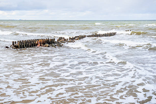 istock Coastal View With Wooden Breakwaters and Rolling Waves Under a Cloudy Sky at the Beach 2225204701