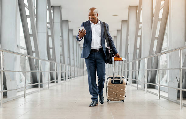 istock Black businessman walking through airport using phone and pulling suitcase 2225205483