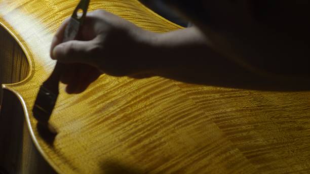 istock Skilled craftsman carefully brushing protective varnish along wooden cello surface, highlighting rich grain details in traditional instrument-making workshop 2225207633
