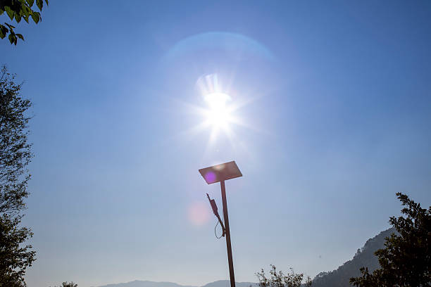 A solar panel illuminated by sunlight amidst a clear, blue sky over a hilly environment. Surrounding trees and mountains enhance the eco-friendly and sustainable energy theme, showcasing harmony with nature.
