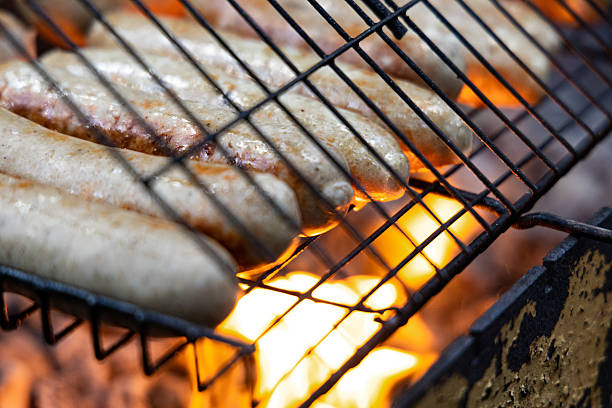 Close-up shot of sausages grilling over an open fire. The meat is sizzling and the flames are visible beneath the grate.