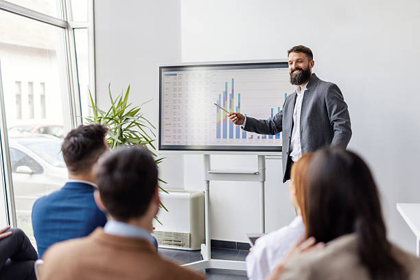 istock Bearded presenter explaining financial report on white board in front of audience. 2225217285
