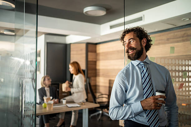 istock Smiling businessman holding coffee cup looking away in modern office 2225218054