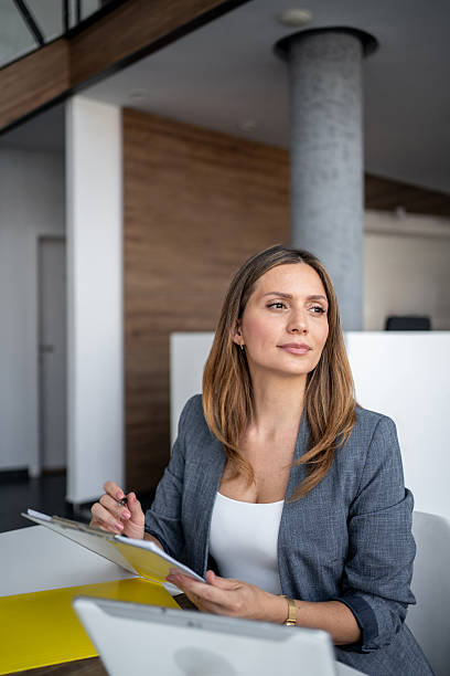 istock Businesswoman holding notes and looking away while sitting at desk 2225219616
