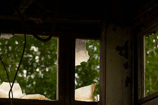 istock A broken window in a dark room offers a view of outside trees 2225219666