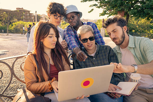 istock Diverse group of students collaborating with a laptop and tablet on a park bench. 2225221551