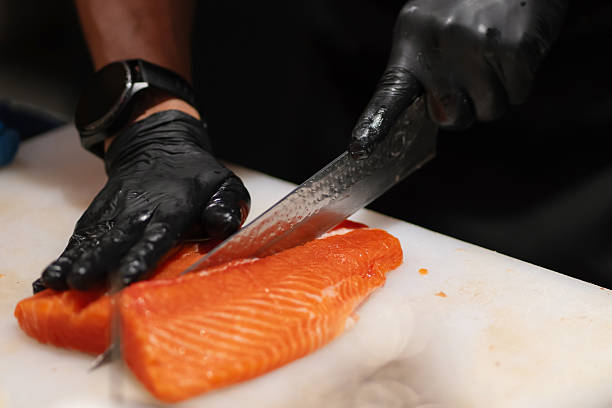 Chef slicing raw salmon fillet on a white cutting board using a sharp knife.