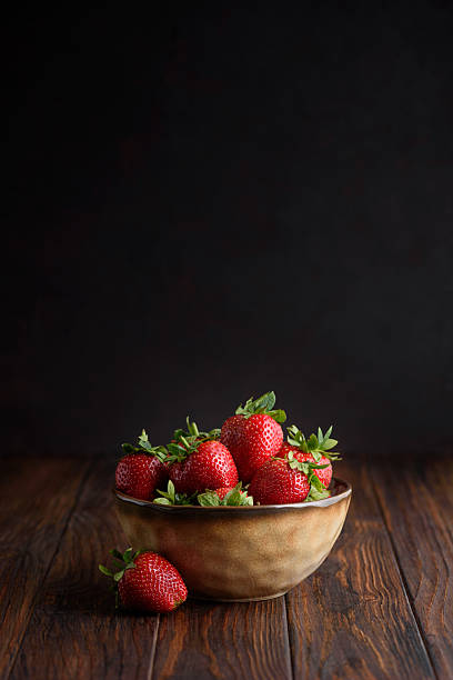 istock Fresh red strawberries in a rustic bowl on a dark wooden background. Front view 2225224212