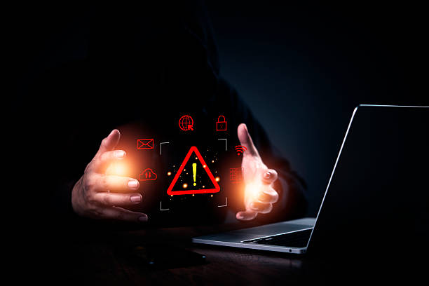 istock hacker in a hoodie with hands protecting a glowing warning icon. Cybersecurity, data breach, and internet security. Cyber attack and network hacking concept. Dark web and illegal activity. 2225225841
