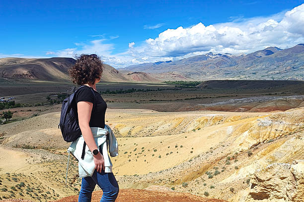 istock Woman stands on a hill with a backpack, looking out over a wide valley, mountain 2225228364