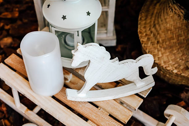 A wooden rocking horse and a lantern rest on a rustic table surrounded by warm decorative elements in a cozy room.