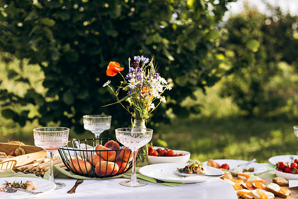Rustic summer picnic table in a garden setting with fresh peaches, strawberries, toast, wildflowers in a glass jar, and vintage glassware. Warm natural light and vibrant colors.