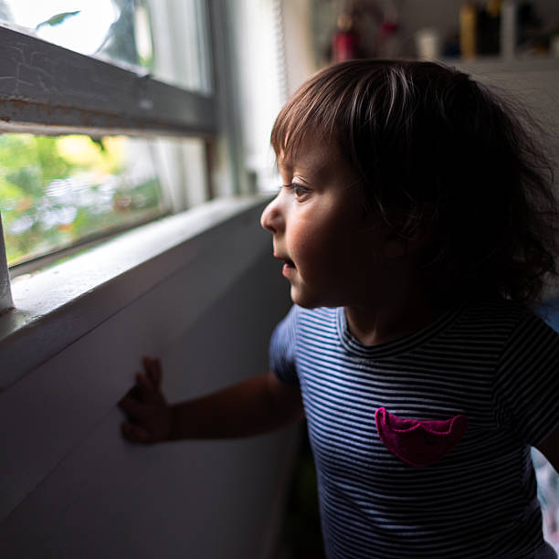 istock Curious Little Girl Looking Out the Window 2225232634