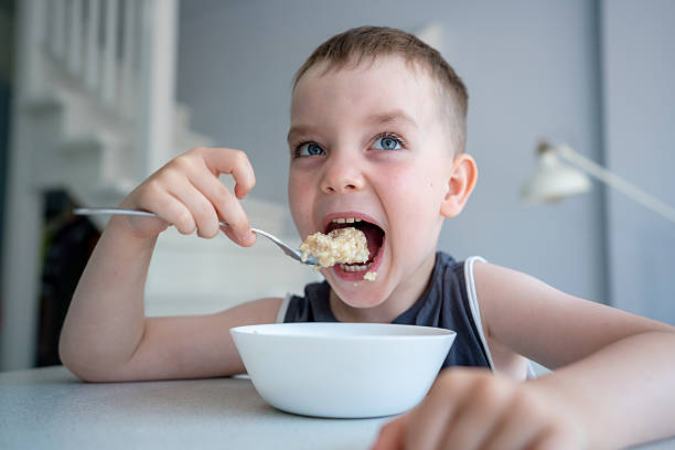 Smiling child eating a bowl of cereal in a bright kitchen environment, demonstrating healthy eating and joy. A candid moment ideal for concepts of childhood happiness and morning routines.