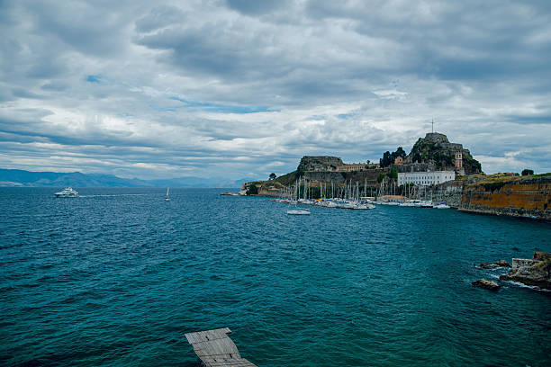 Scenic view of a coastal fortress with yachts and cloudy sky.