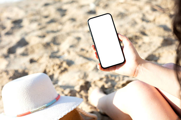 istock A woman holding black mobile phone with blank desktop screen while sitting on a beach 2225242163