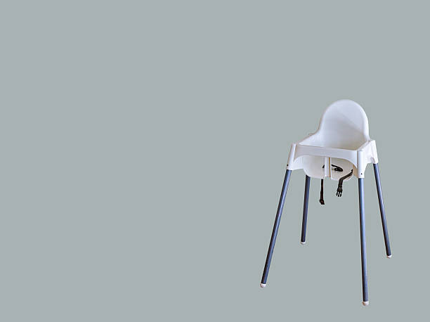 A minimalistic white baby high chair with metal legs stands alone against a solid gray background