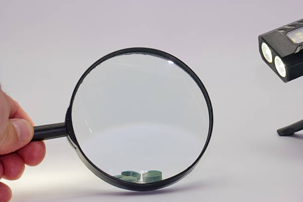 istock Magnifying glass held by a person near a light source and small objects on a surface in a well lit environment 2225247532