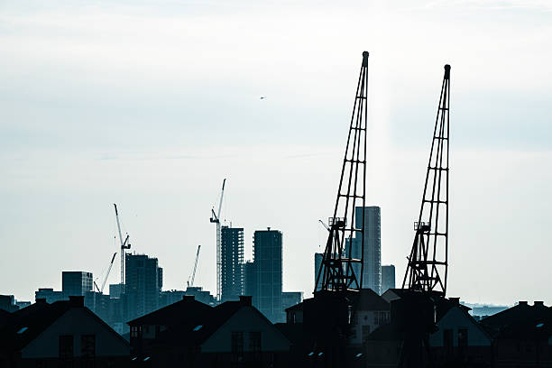 Silhouetted cranes dominate the skyline of london's east end, symbolizing urban development and industrial activity