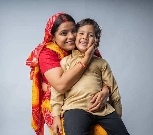 Portrait of loving mid adult mother in sari embracing cute son while sitting against white background
