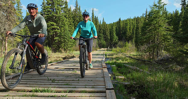 istock Front view of mature couple riding e-bicycles on boardwalk in forest 2225252324