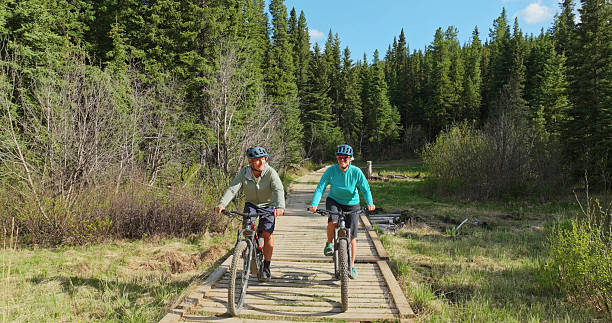 istock Front view of mature couple riding e-bicycles on boardwalk in forest 2225252326