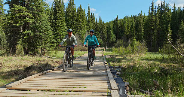 istock Front view of mature couple riding e-bicycles on boardwalk in forest 2225252327