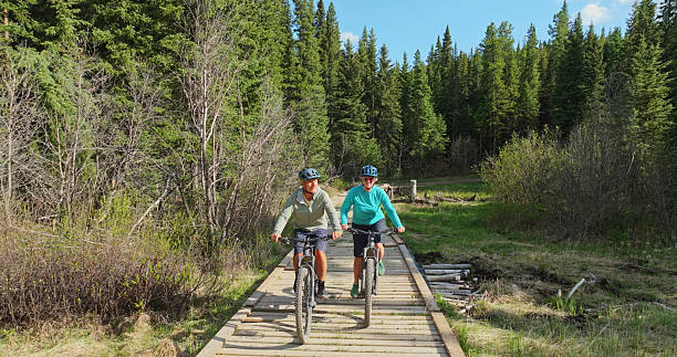 istock Front view of mature couple riding e-bicycles on boardwalk in forest 2225252328