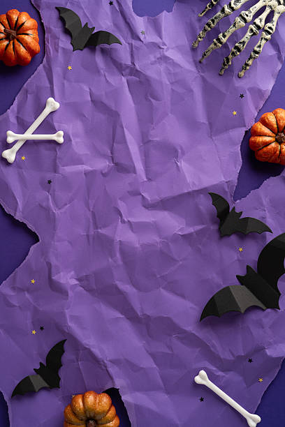 istock Halloween-themed vertical flat lay with decorative elements including bats, pumpkins, bones, and stars placed around a purple textured backdrop creating a spooky and festive atmosphere 2225270798