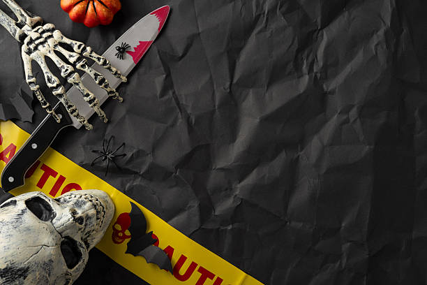 istock Eerie Halloween composition featuring skeleton hand, skull, caution tape, spider, bat, and knife on crumpled black paper background 2225270823