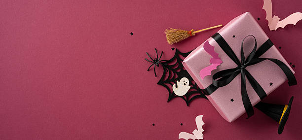istock Halloween-themed pink gift box with decorations including bats, a broomstick, spider web, and stars 2225270828