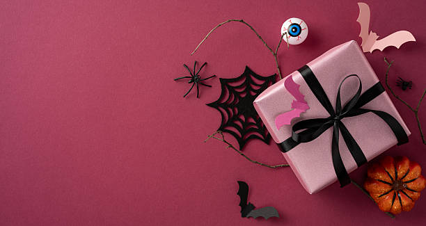 istock Colorful Halloween arrangement featuring a wrapped gift box adorned with festive decorations, showcasing bats, webs, and pumpkins, all against a vibrant red backdrop 2225270837