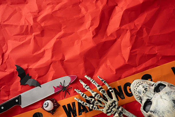 istock Halloween inspired composition with various decorations, including skeleton hand, warning tape, and knife, complemented by a festive red background 2225270839
