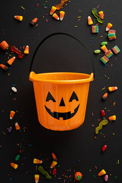 istock Festive vertical Halloween candy display with an orange pumpkin bucket on a black surface surrounded by sweets 2225270847