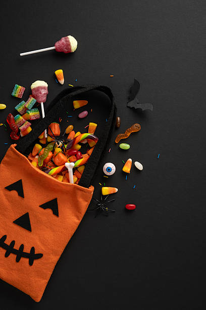 istock Halloween vertical trick-or-treat bag with assorted candies, lollipops, and decorations lying scattered around 2225270850