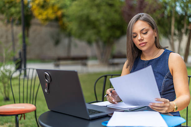 istock Young woman analyzing financial documents at desk with laptop while working in home office, focusing on tasks in an organized and productive environment. 2225275945