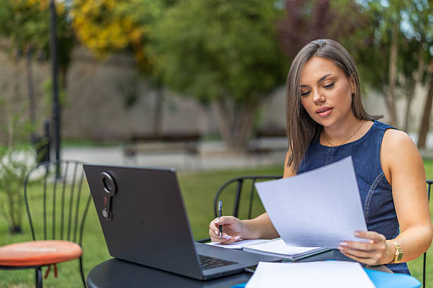 istock Young female employee watching at the screen and taking notes, watching webinar and writes down outdoor. 2225275954