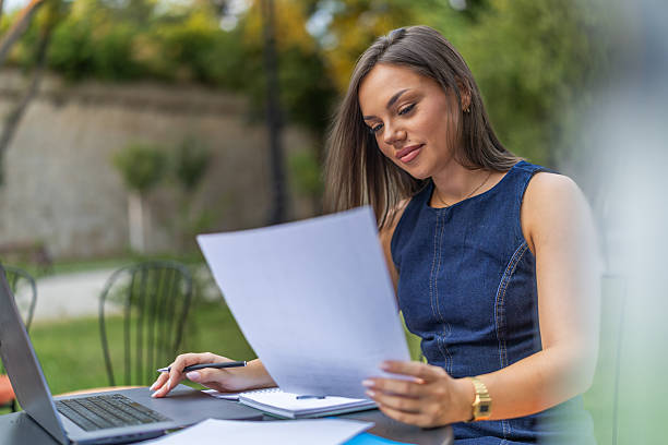 istock Young woman analyzing financial documents at desk with laptop while working in home office, focusing on tasks in an organized and productive environment. 2225275988