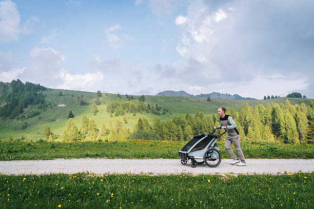 Father pushes baby in stroller up mountain pathway, in springtime on a moody day, Dolomites