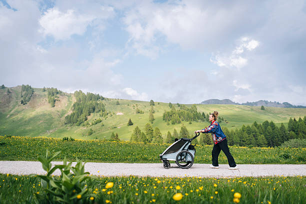 Mother pushes baby stroller on mountain road, distant view, springtime, Dolomites
