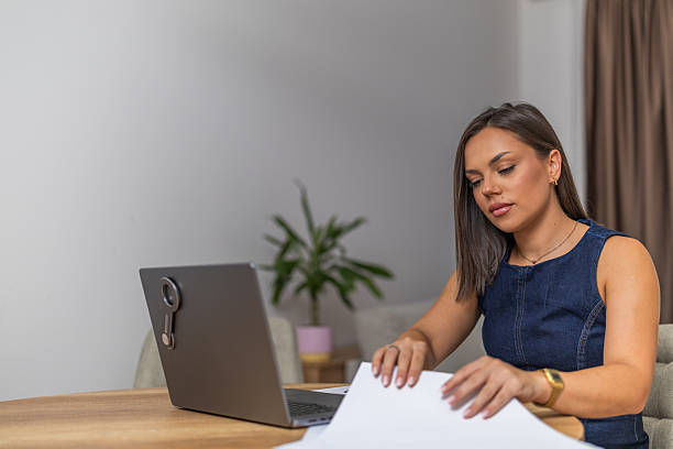 istock Young woman analyzing financial documents at desk with laptop while working in home office, focusing on tasks in an organized and productive environment. 2225276379